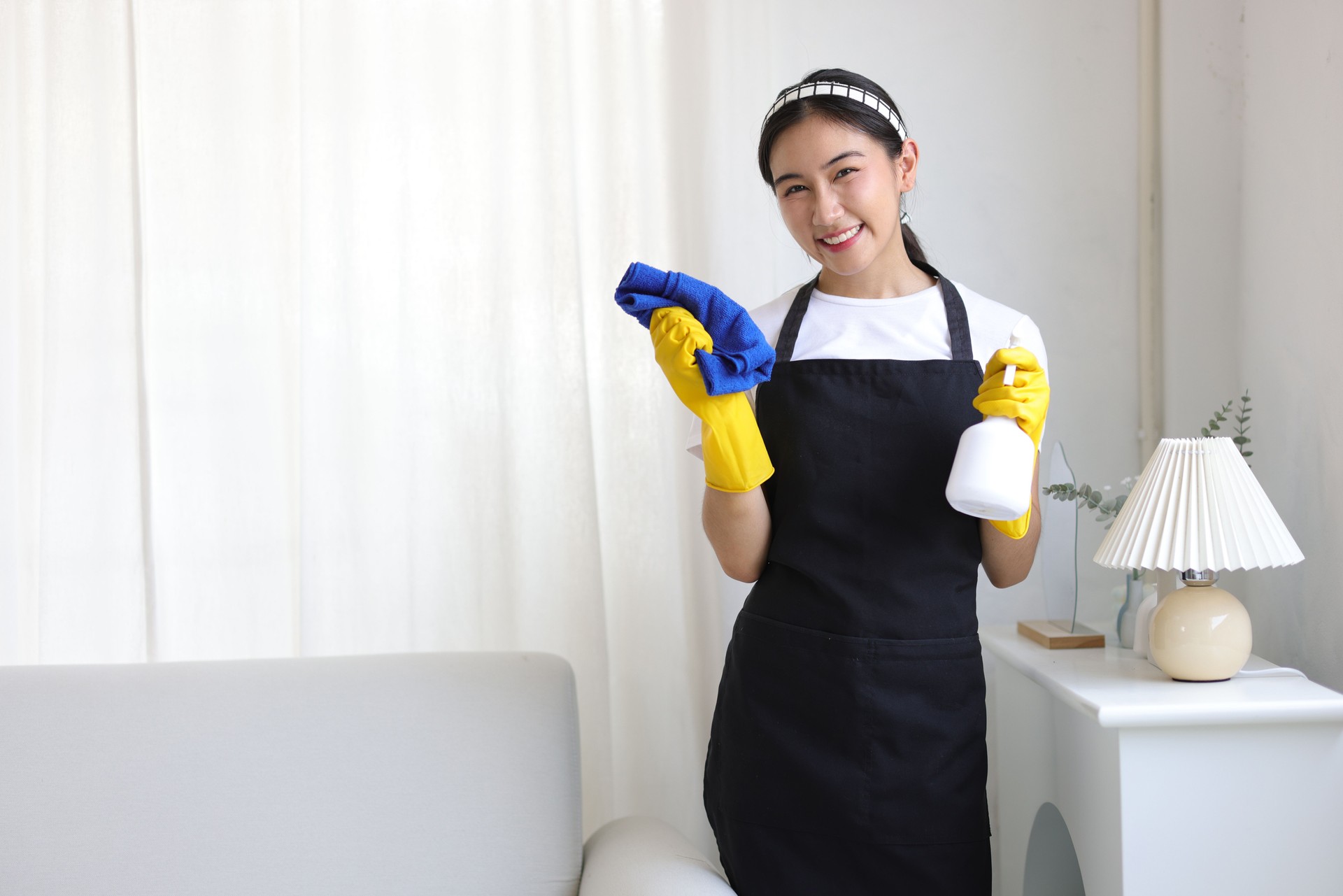 Young woman cleaning the house holds a spray bottle of disinfectant and a wiping towel.