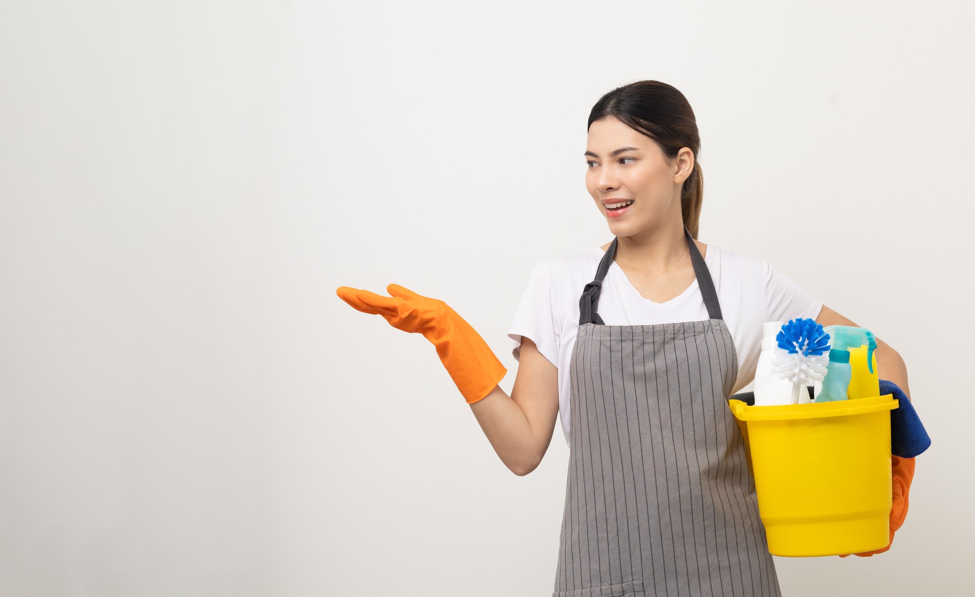 Young housekeeper woman holding bucket of cleaning products ready for cleaning home on isolated white background.
